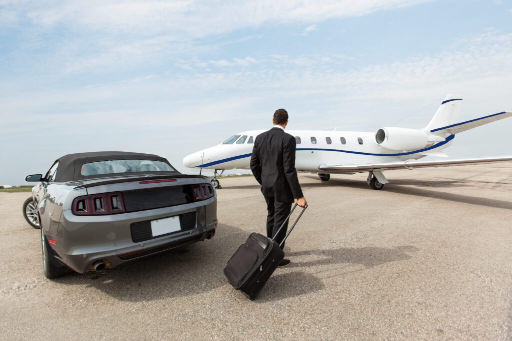Businessman with luggage standing by car and private jet at airport terminal